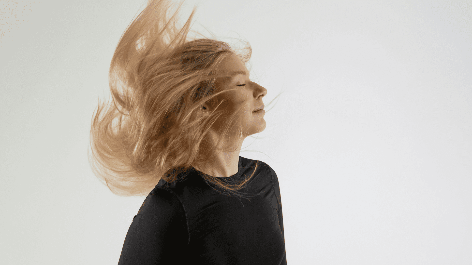 Person in black shirt flipping their long blond hair against a plain background.