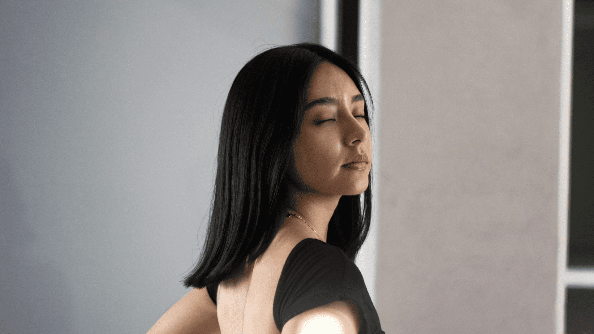 Woman with long dark hair standing with closed eyes, wearing a black top.